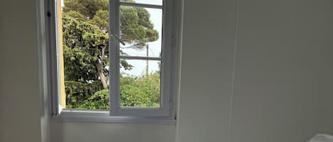 Ein Schlafzimmer mit einem Bett, einem Fenster und Blick auf Bäume.