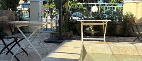 A pool area with a table and chairs, surrounded by a fence and greenery.