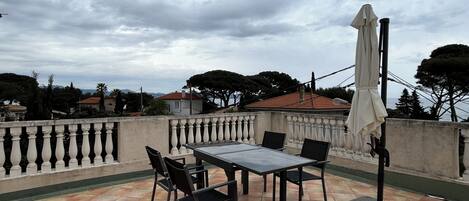 An outdoor patio with a table and chairs, a covered umbrella, and a view of the surrounding area.