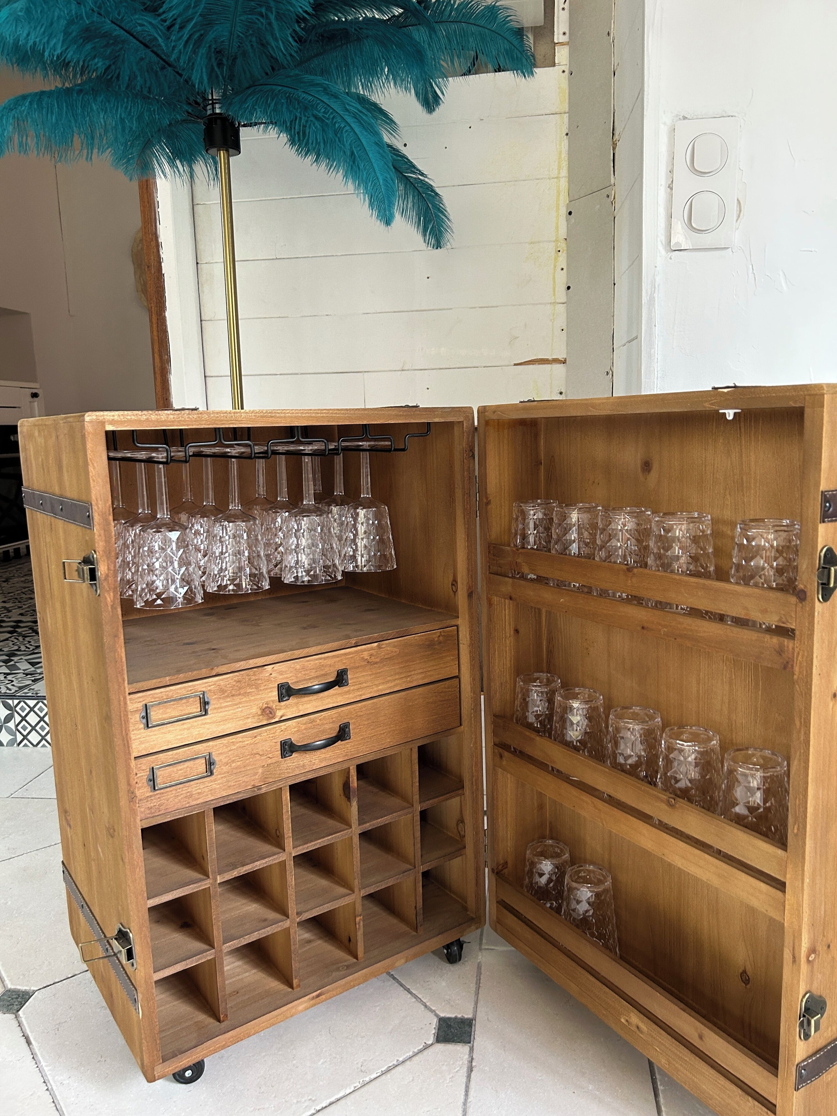Un meuble en bois doté de plusieurs étagères et tiroirs, contenant de la verrerie transparente et des objets décoratifs.