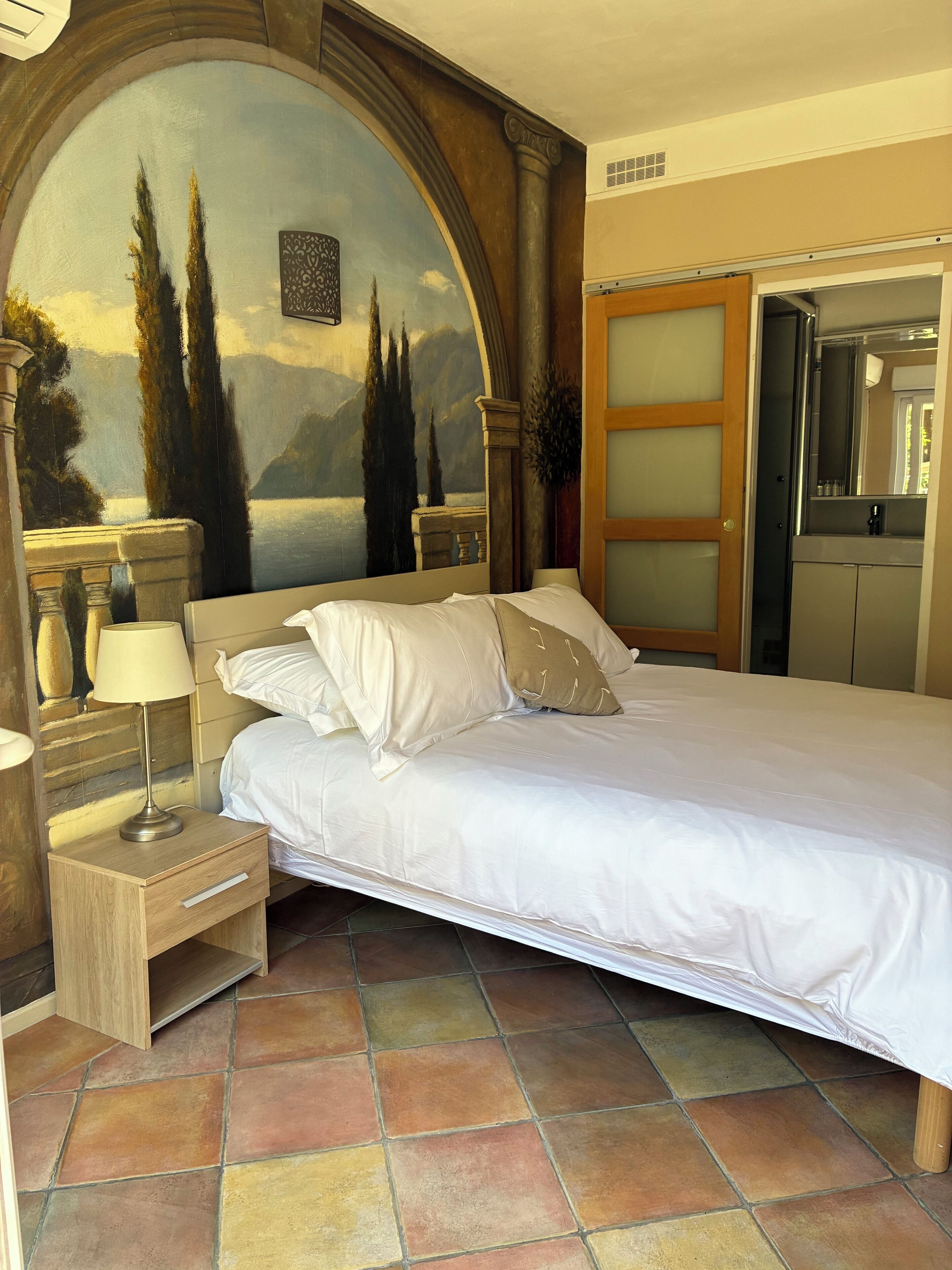 A bedroom with a bed, nightstand, lamp, and a painting above the bed.