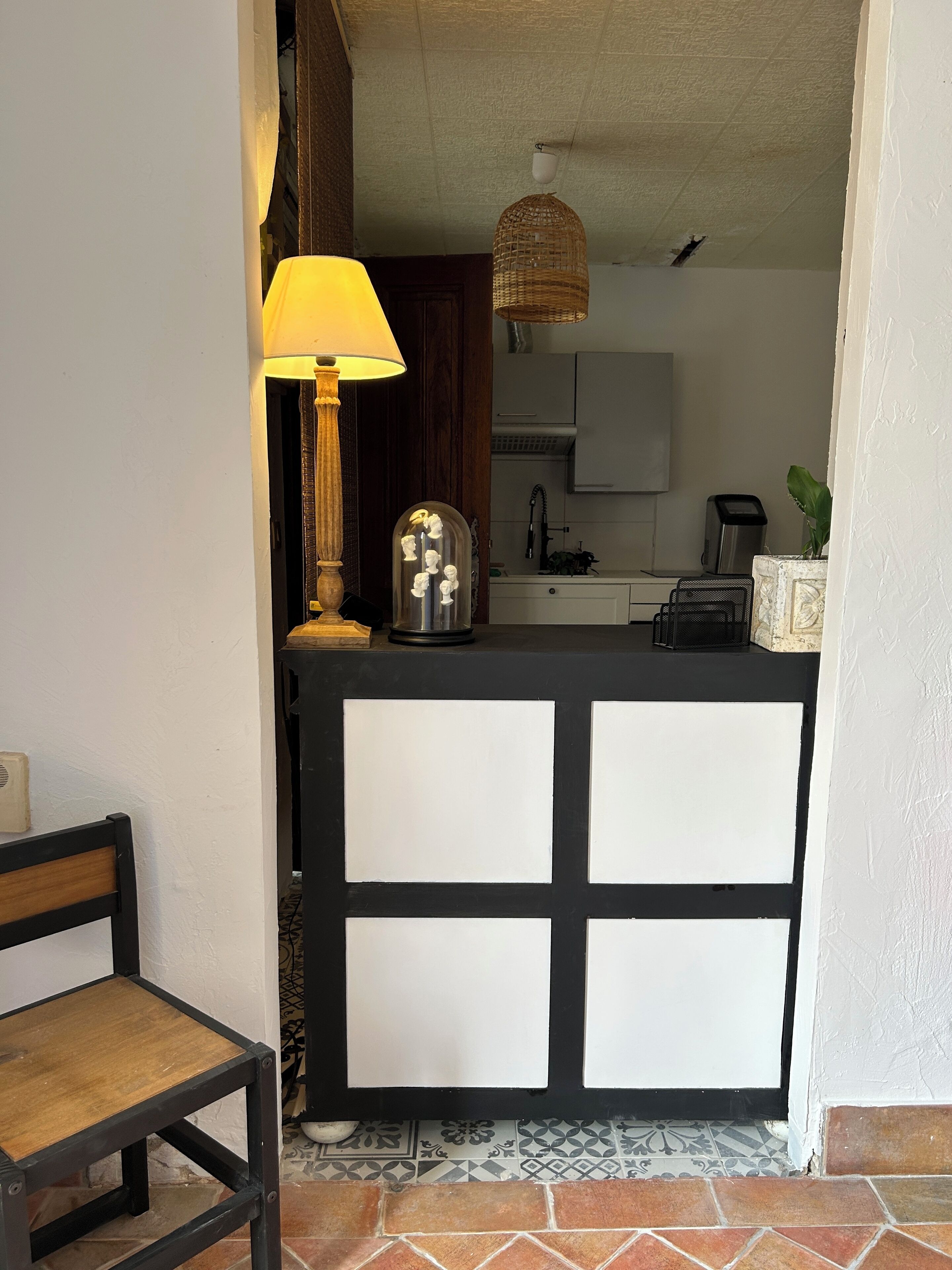 Une cuisine compacte avec un revêtement mural noir et blanc, un luminaire suspendu et un petit îlot central surmonté d’un dôme en verre.