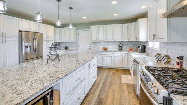 A modern kitchen with white cabinets, granite countertops, stainless steel appliances, and pendant lighting. - Charming 5-bedroom Cadillac Retreat W/ Private Hot Tub Shared Basketball Court (Cadillac)