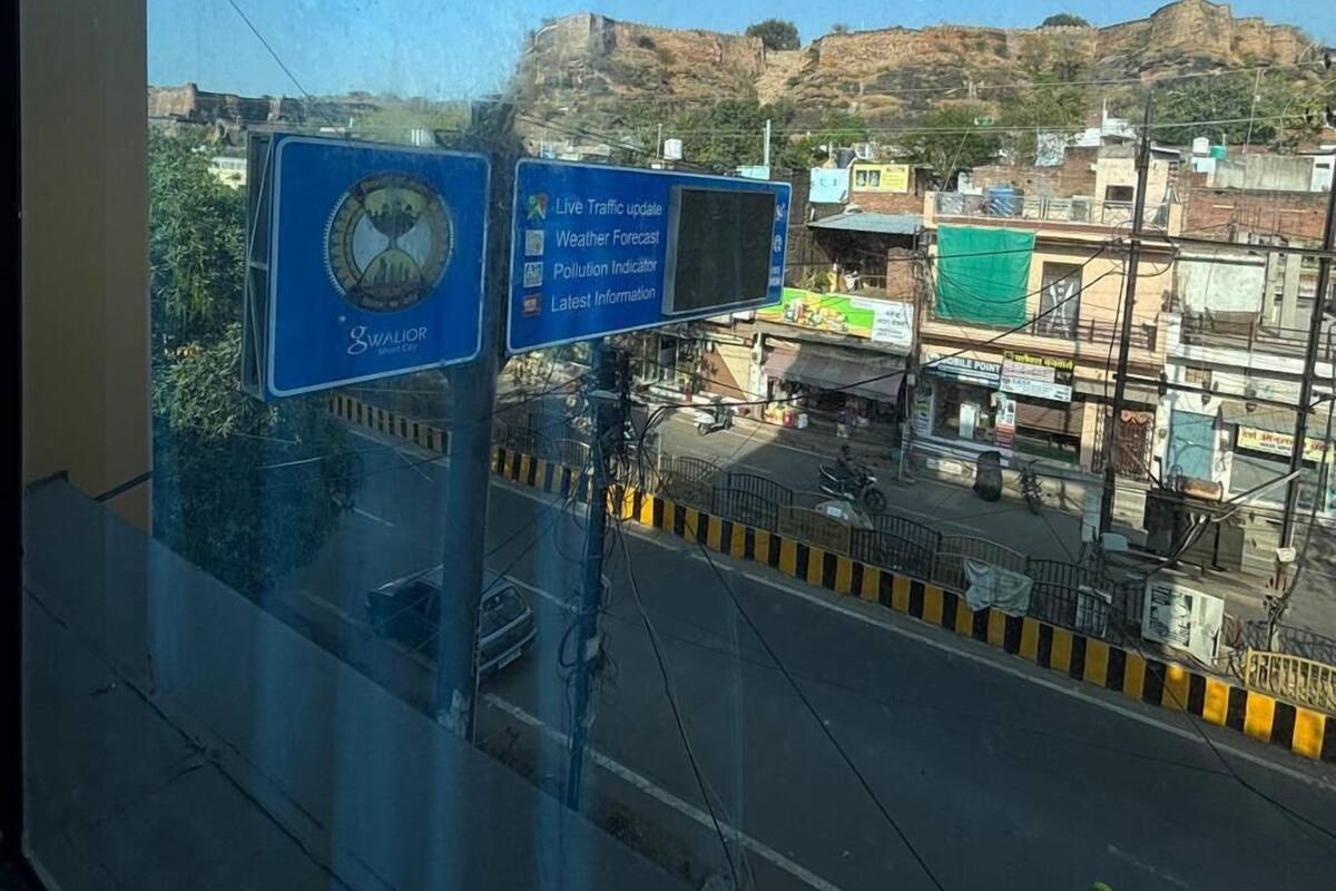A view from inside a building with a large window overlooking a busy street. There are signs indicating live traffic updates, weather forecast, pollution indicators, and latest information.