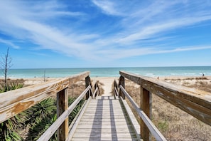 Une promenade en bois menant à une plage, avec un ciel dégagé.