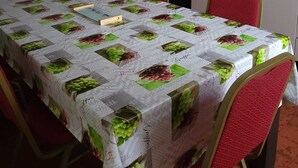 A dining area with a table covered in a grape-themed tablecloth, red chairs, a white refrigerator, and a black TV mounted on the wall. - SPACIOUS 3-BEDROOM APT (APT N°15) (Roanne)