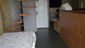 A room with a spiral staircase, a bed with a floral bedspread, a tiled floor, a kitchen area, and a counter with towels.
