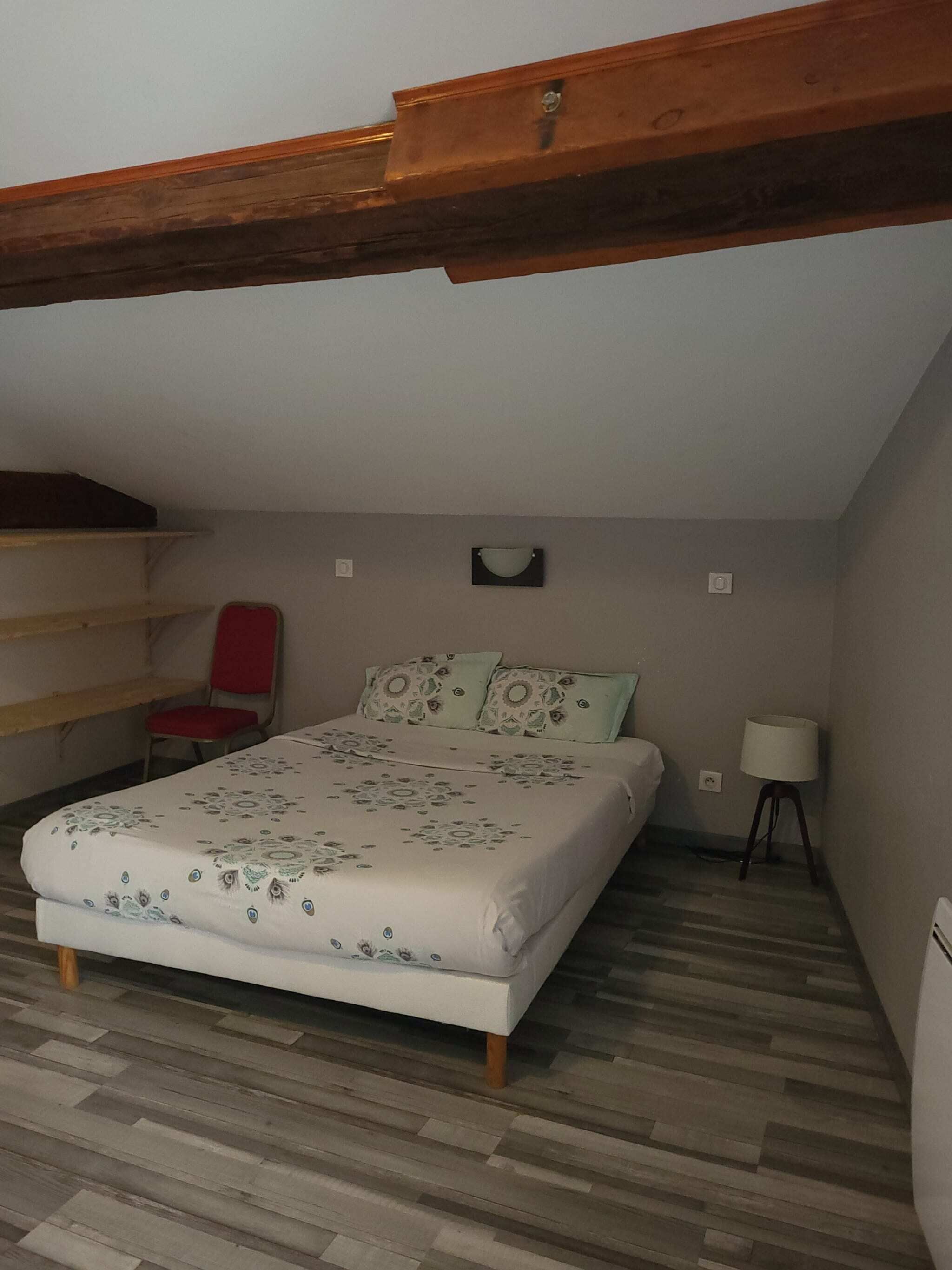 Quarto com uma cama, uma cadeira, um abajur e uma estante.