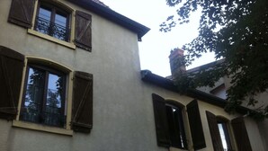 Un edificio con varias ventanas, algunas con persianas, y un árbol visible a la derecha.