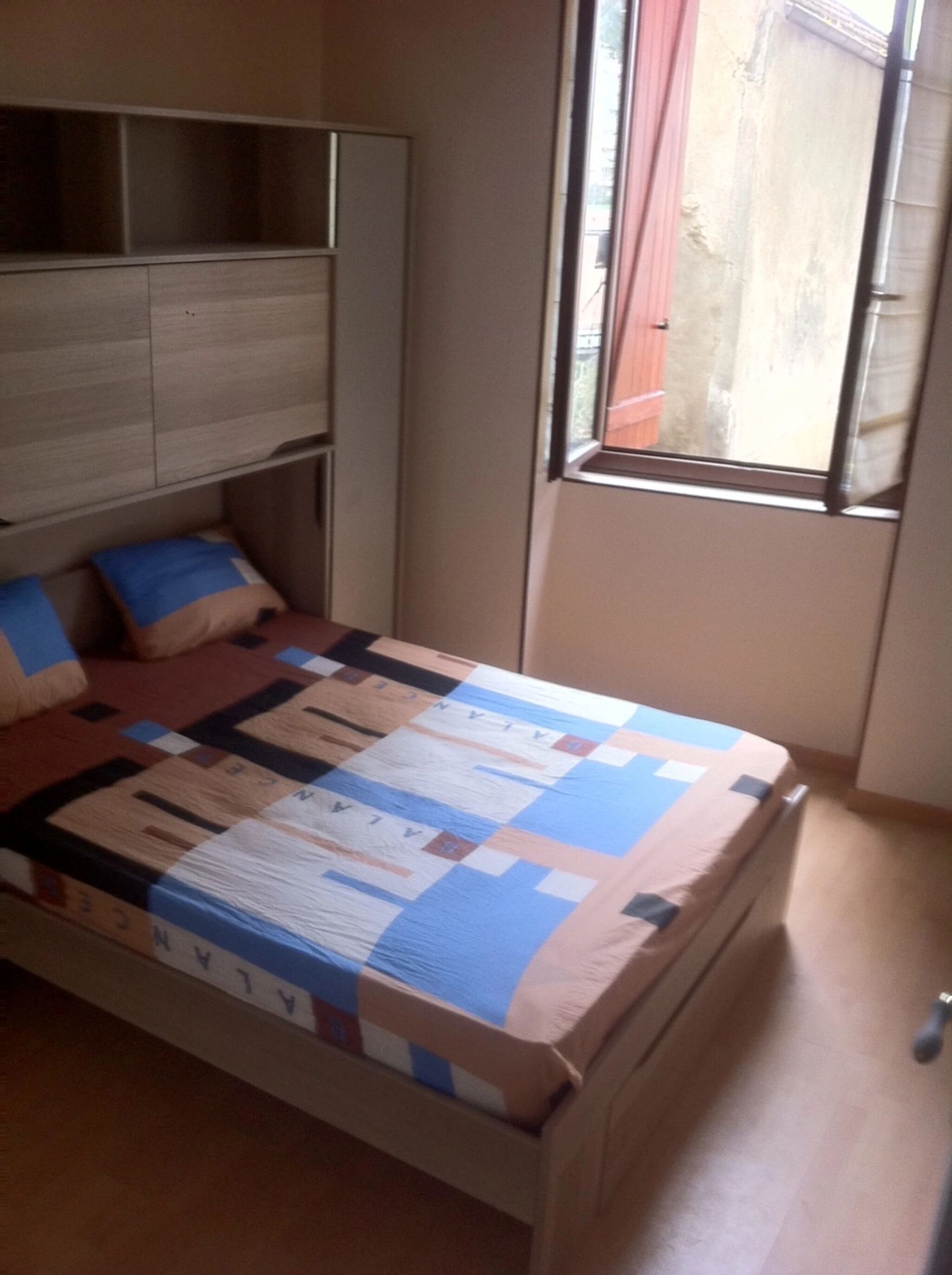 A bedroom with a bed, a headboard, a window, and a view of the outside.