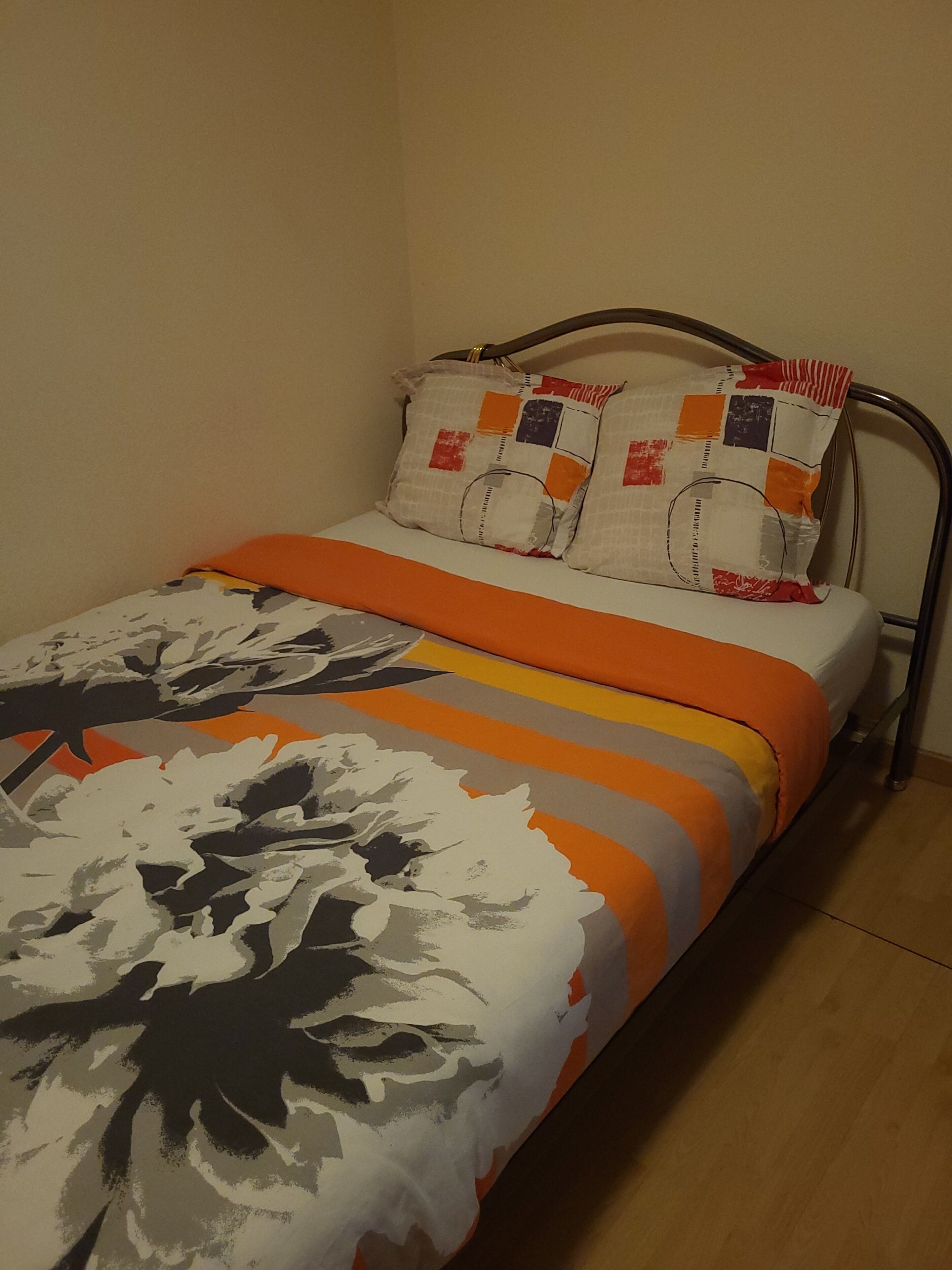 A single bed with a patterned bedspread, two pillows with a patchwork design, and a metal headboard.