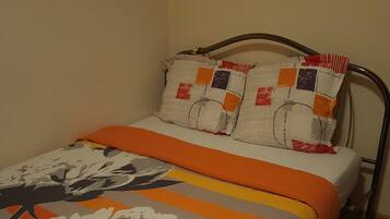 A single bed with a patterned bedspread, two pillows with a patchwork design, and a metal headboard.