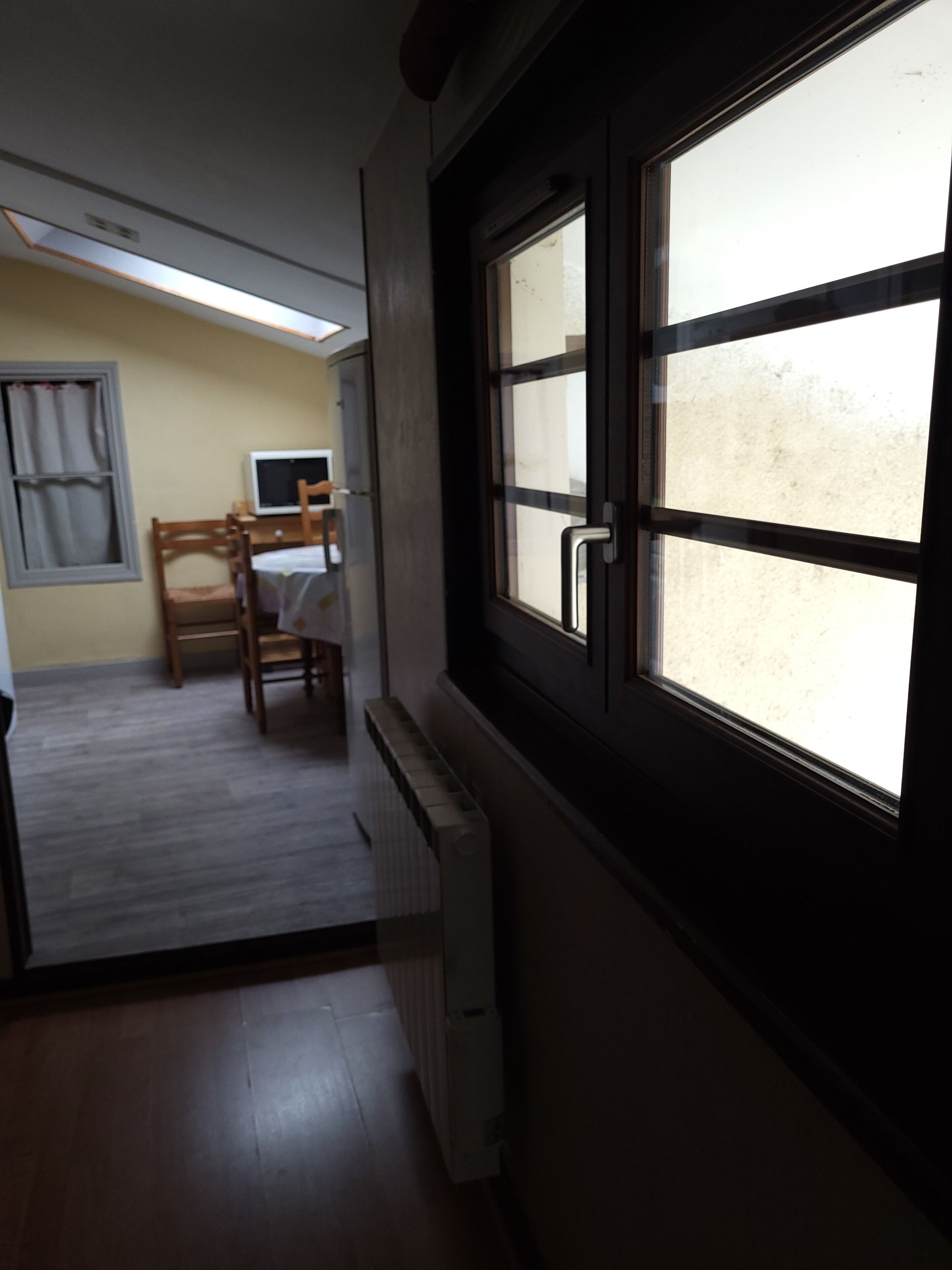 A narrow hallway with a window on the right, a radiator on the left, and a dining area in the background.