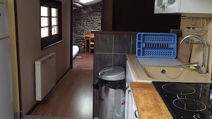 A narrow kitchen with a built-in stove, a sink, and a trash bin. There is a window on the left and a stone wall in the background. - SUITE EN BORD DE LOIRE (APT N°23) (Roanne)
