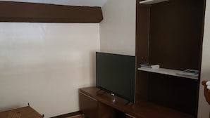 A compact living space with a television on a wooden stand, a small table with a mat, a wicker bench, and a shelving unit against the wall. - SUITE EN BORD DE LOIRE (APT N°23) (Roanne)