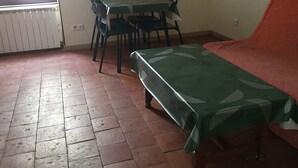 Una stanza con pavimento piastrellato, un tavolo verde con sedie, un divano e un termosifone.