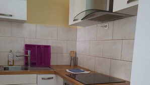 Una cucina compatta con mobili bianchi, una cappa in acciaio inossidabile, un espositore per piatti viola e un forno integrato.