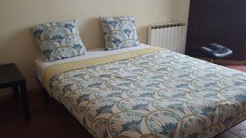 Un lit recouvert d’une couvre-lit à motifs floraux, deux oreillers assortis, une table de chevet et un radiateur.