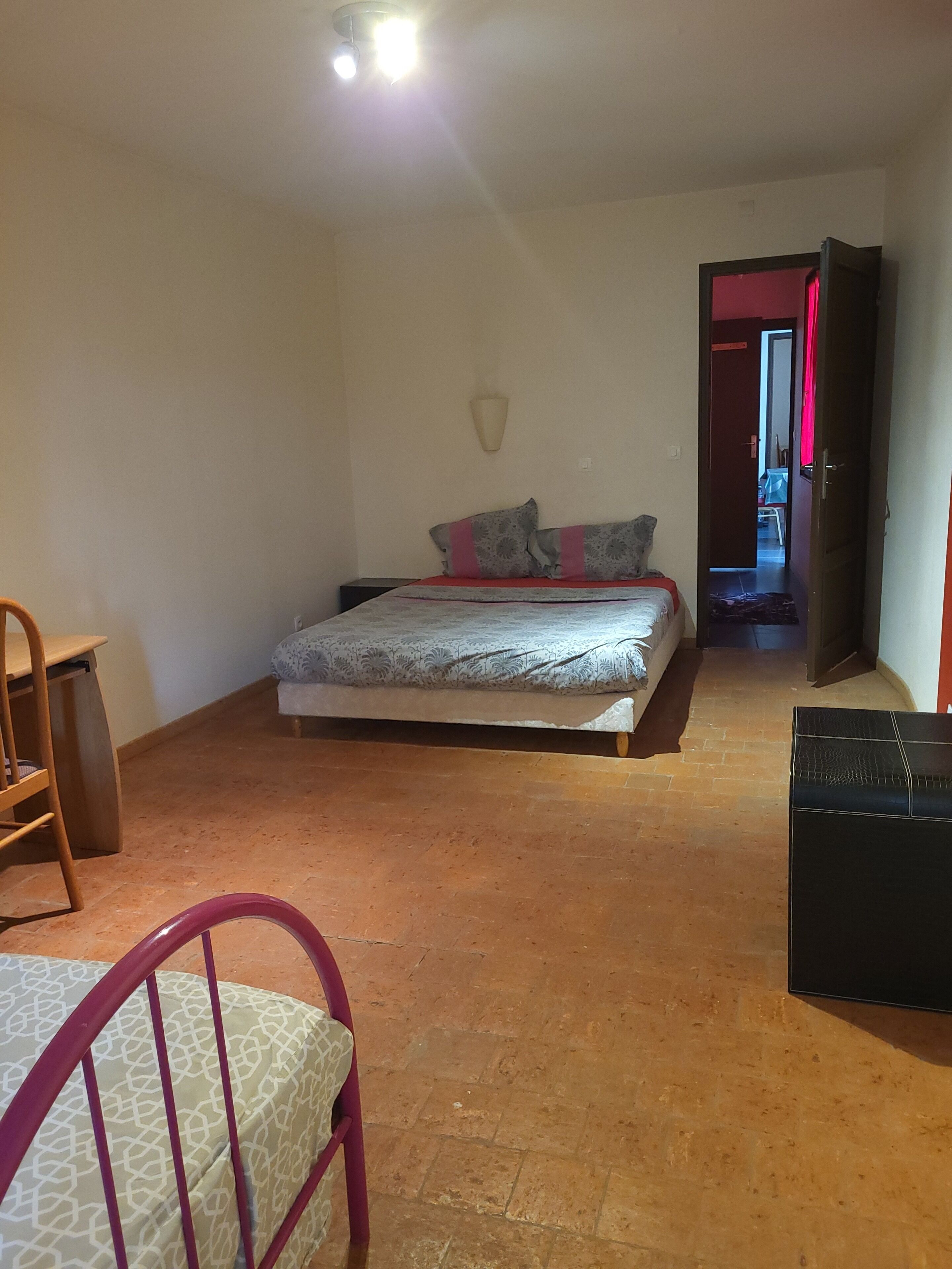 Ein Schlafzimmer mit einem Bett, einem Sessel, einem Kleiderschrank und einer Tür zu einem weiteren Raum.