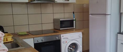 A compact kitchen with a microwave, oven, and washing machine.
