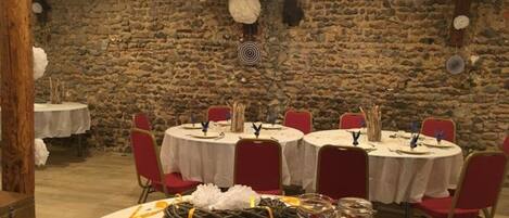 Un coin repas au décor rustique, avec des murs en pierre, des tables rondes et des chaises rouges.