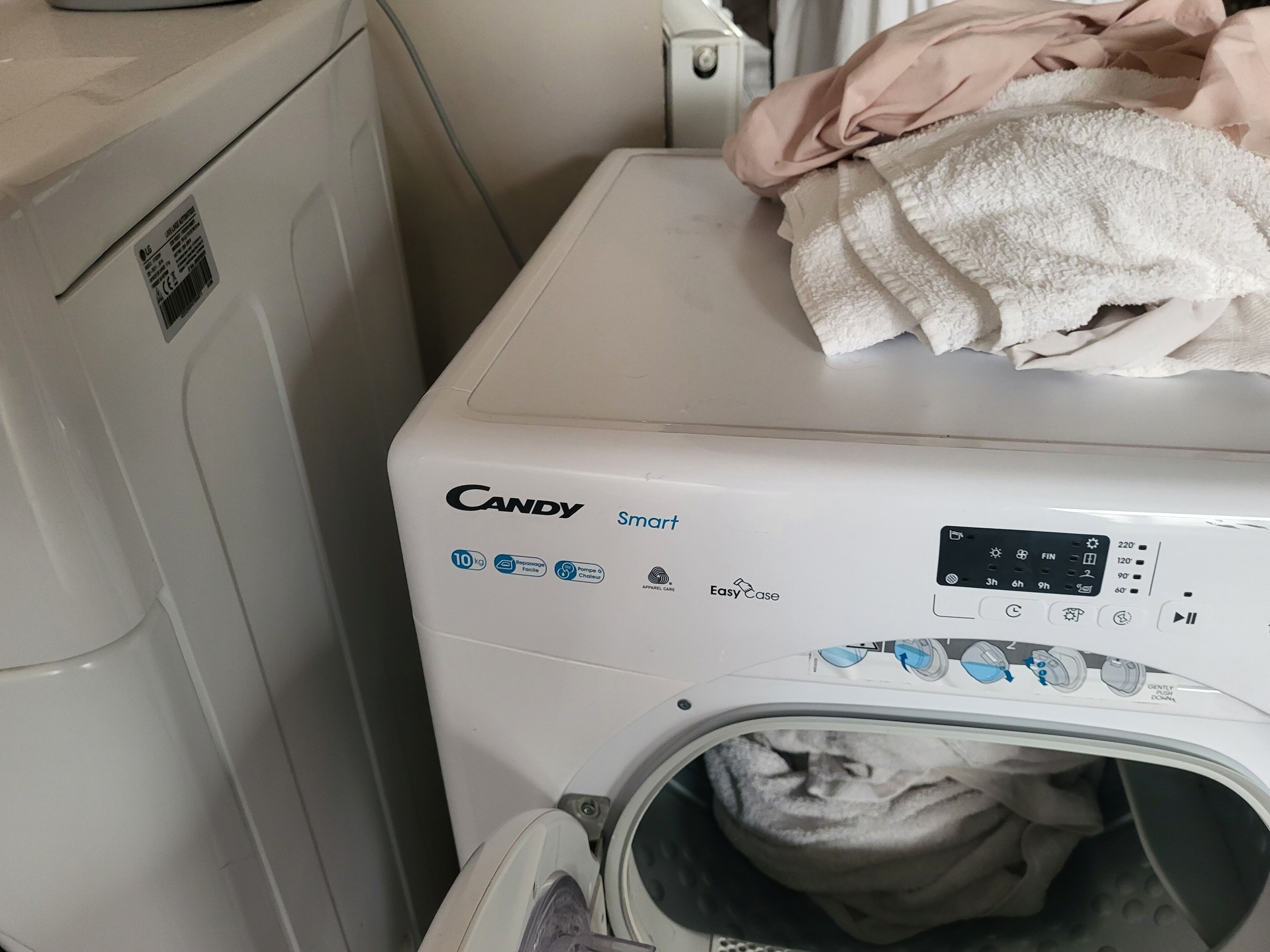 En tvättmaskin med frontmatning, ett kontrollpanel, ett vitt hölje och en hög med vita handdukar ovanpå.