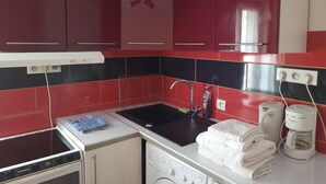 Une cuisine avec des meubles de couleur rouge, un évier noir, un lave-linge et une machine à café.