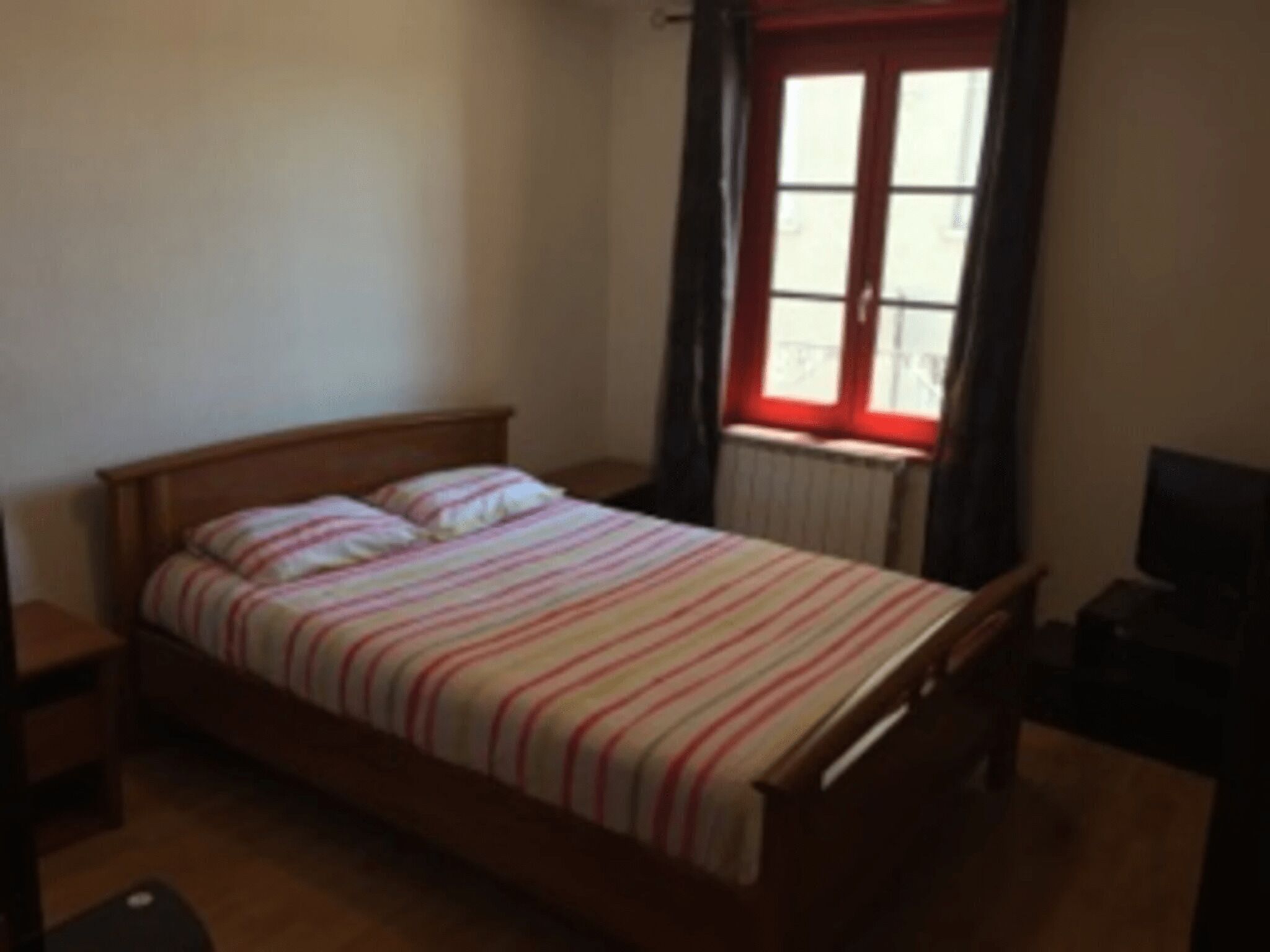 A single bed with a striped bedspread in a room with a window and a radiator.