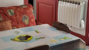 Un coin repas avec une table dressée pour deux personnes, une porte rouge et un radiateur.