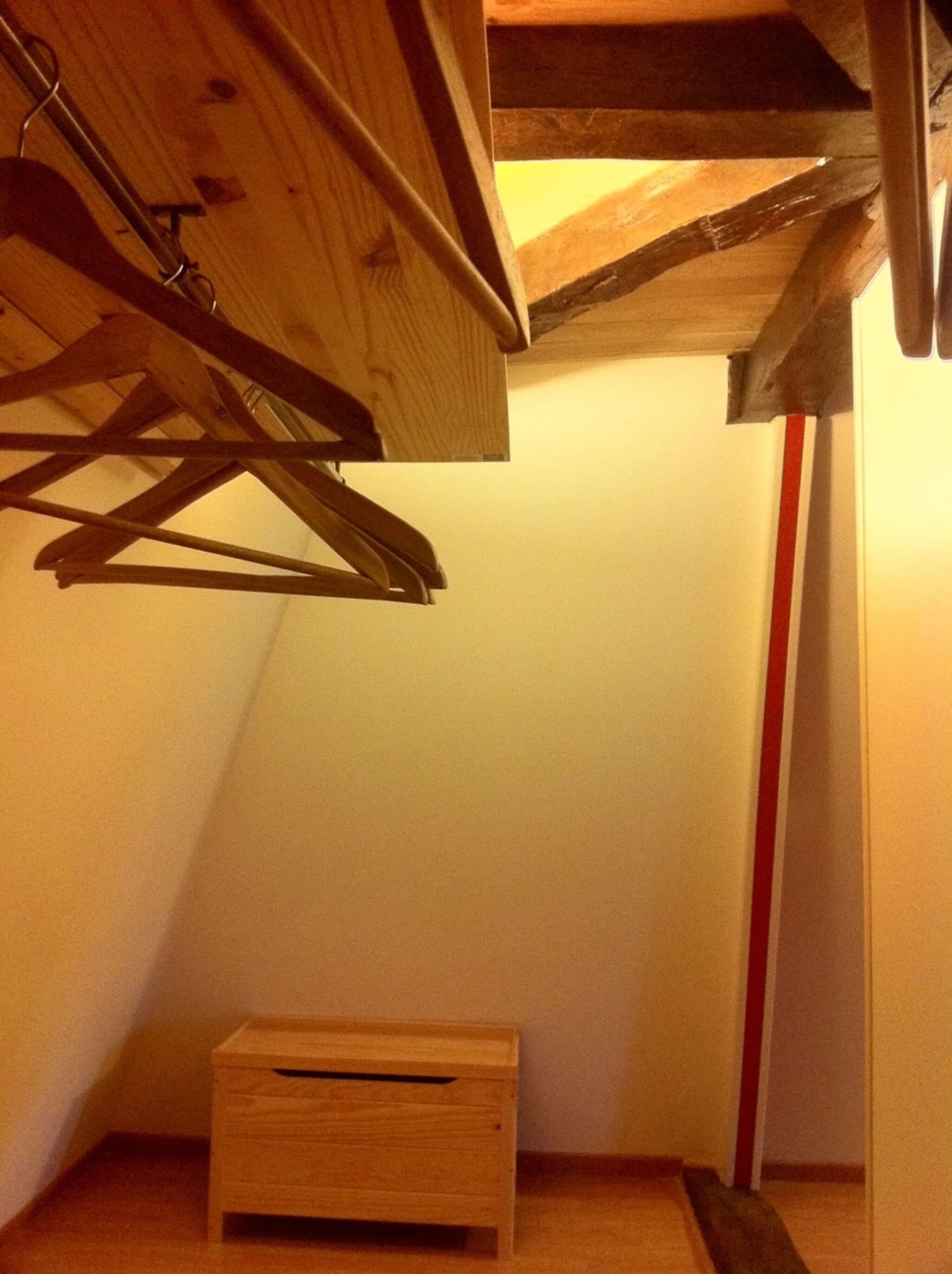 Un racó d'una habitació amb terra de fusta, una paret amb franges vermelles i blanques i una petita caixa de fusta.
