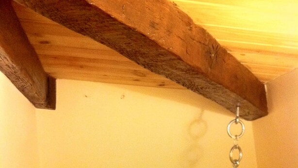 Une pièce avec une poutre en bois au plafond, un mur blanc et un portant métallique avec des cintres.