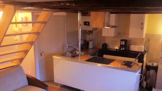 A compact kitchen with a built-in island, a sofa, and a staircase leading to an upper level. - DUPLEX UNDER THE SLOPES ON THE BANKS OF THE LOIRE (APT N°22) (Roanne)