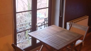 A small room with a wooden table and two chairs, a window with a view of trees and a car, and a radiator on the wall. - DUPLEX UNDER THE SLOPES ON THE BANKS OF THE LOIRE (APT N°22) (Roanne)