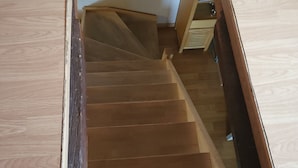 A wooden staircase with a handrail, leading to a landing with a white wall and a small window. - DUPLEX UNDER THE SLOPES ON THE BANKS OF THE LOIRE (APT N°22) (Roanne)