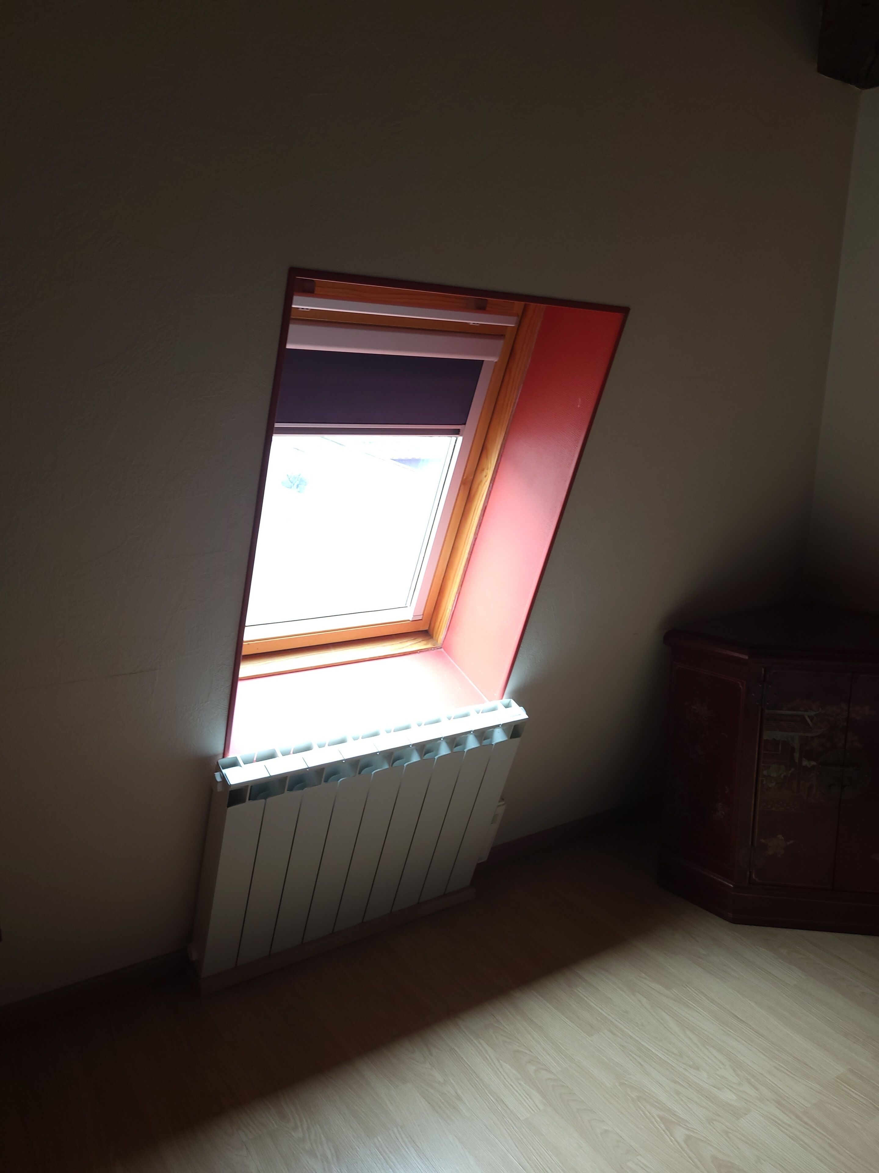 Ein Zimmer mit geneigter Decke, einem Fenster mit Blick, einem Heizkörper und einem Holzschrank.