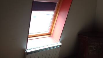 Ein Zimmer mit geneigter Decke, einem Fenster mit Blick, einem Heizkörper und einem Holzschrank.