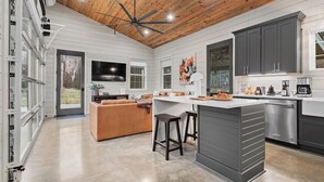 Une cuisine spacieuse dotée d’un grand îlot central, de meubles de couleur sombre et d’un ventilateur de plafond moderne.