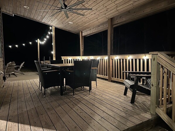 A wooden deck with a table and chairs, string lights, and a wooden railing.