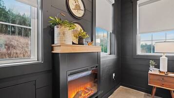 A room with a fireplace, a shelf with decorative items, and a window with a view of trees.