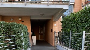 A narrow pathway leading to a building entrance with a metal gate, a small planter, and a metal fence on one side. - Cassino-two-room apartment-park rondo (Cassino)