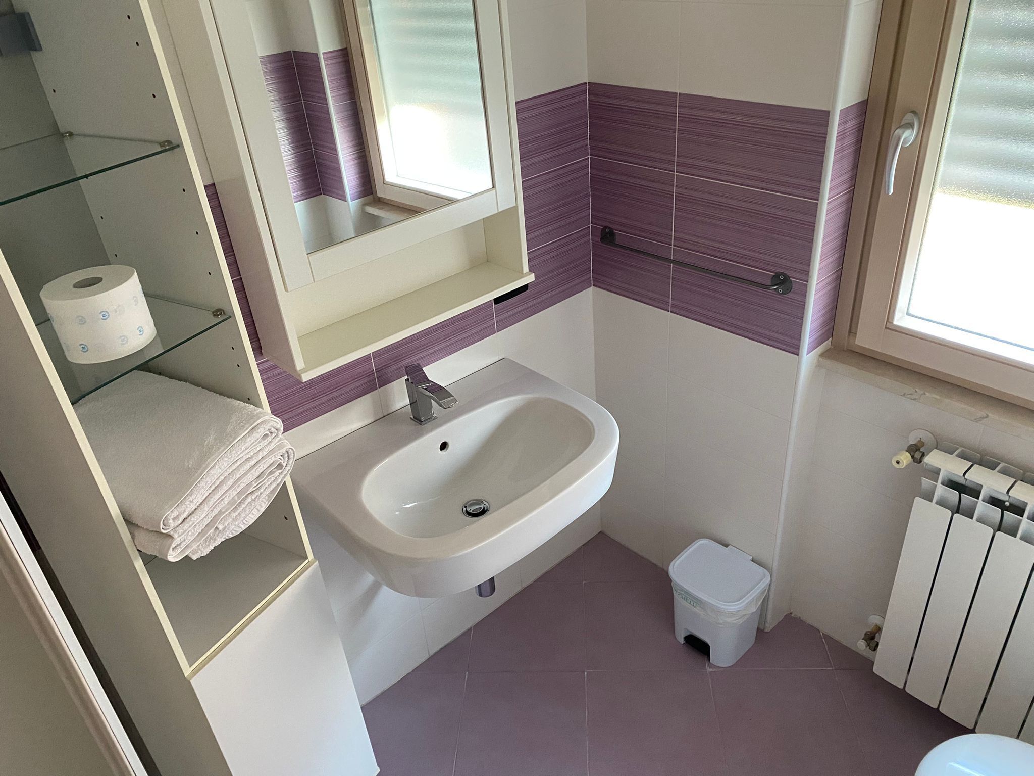 Ein Badezimmer mit Waschbecken, Spiegel, Toilette und einem kleinen Mülleimer.