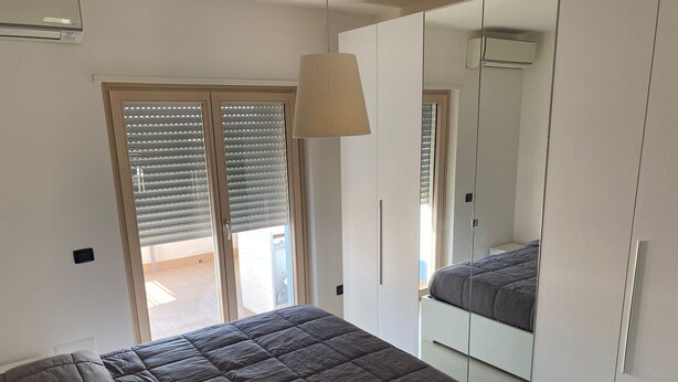 A bedroom with a bed, a wardrobe, and a sliding door to a balcony. - Cassino-two-room apartment-park rondo (Cassino)