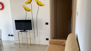 A living room with a sofa, a TV on a stand, and a door. - Cassino-two-room apartment-park rondo (Cassino)