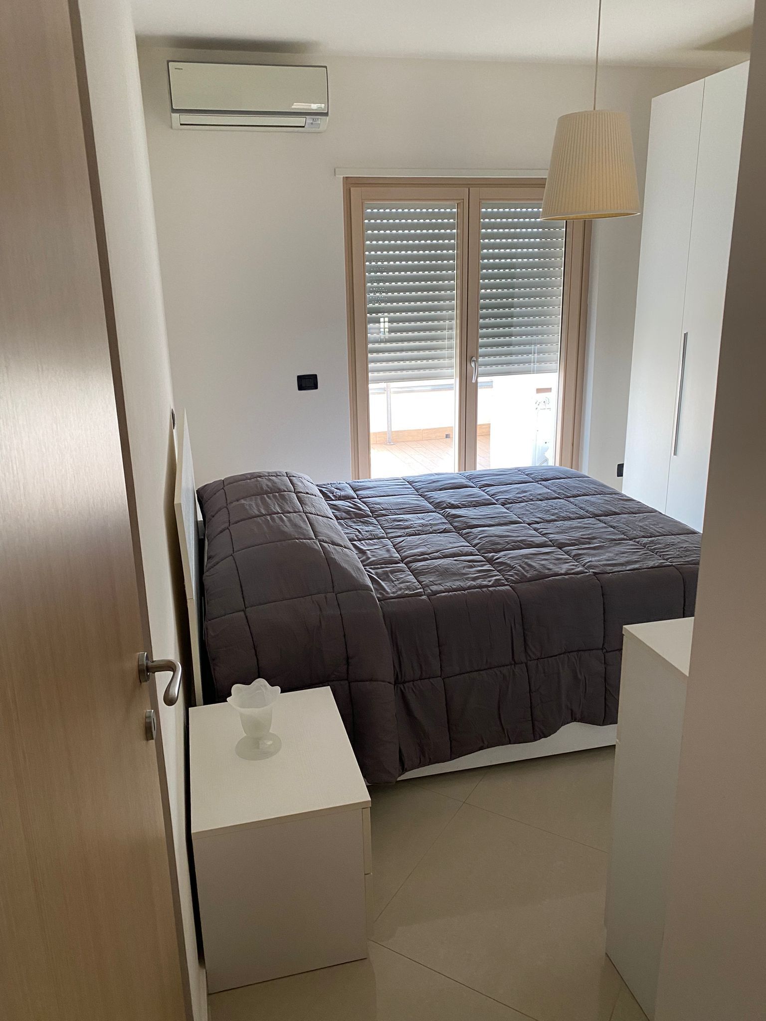 Une chambre à coucher comprenant un lit, une table de chevet, une armoire et une fenêtre avec des stores.