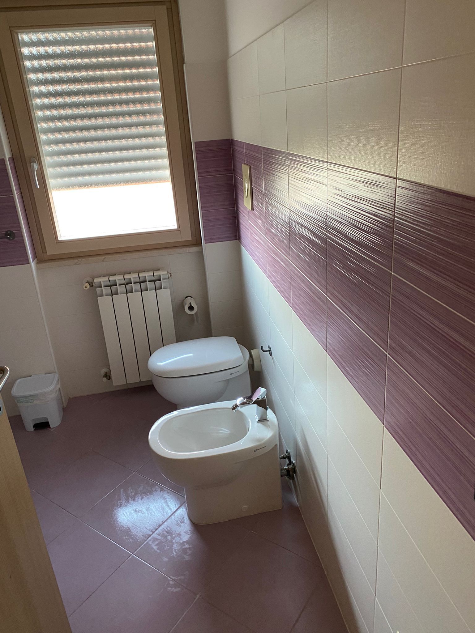 Une salle de bain équipée de toilettes, d’un bidet et d’une fenêtre avec stores.