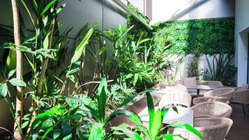 Un espacio patio con mobiliario de mimbre y abundante follaje, incluyendo plantas altas y un muro jardín vertical.