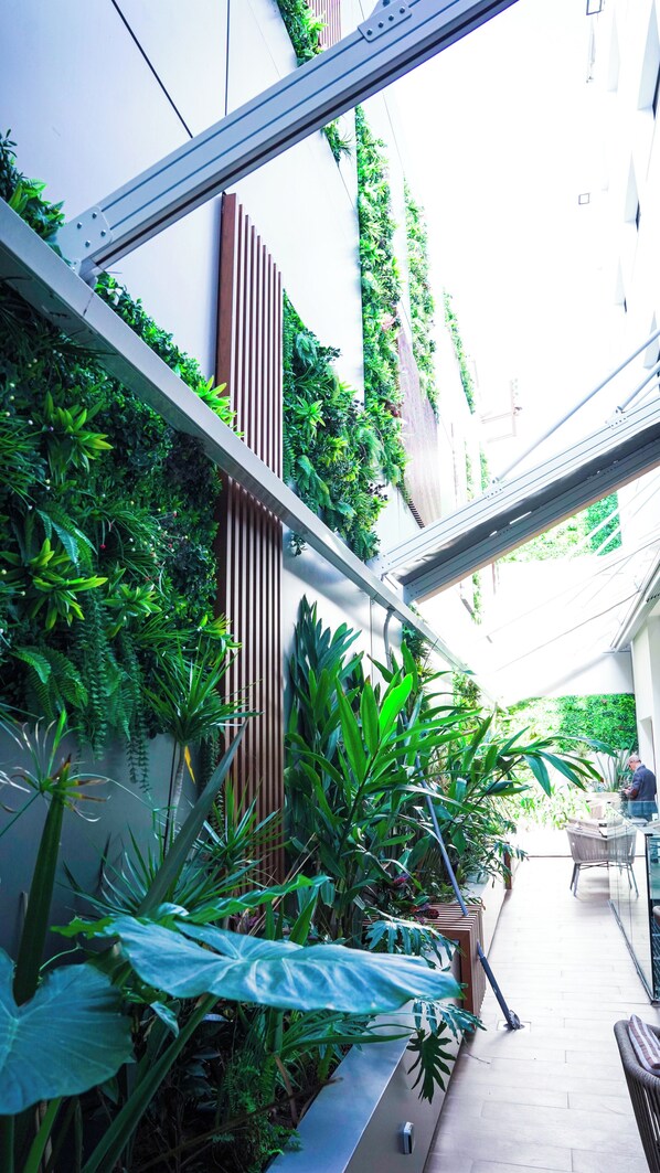 A narrow outdoor corridor with vertical gardens, a metal beam structure, and a seating area with a table and chairs.