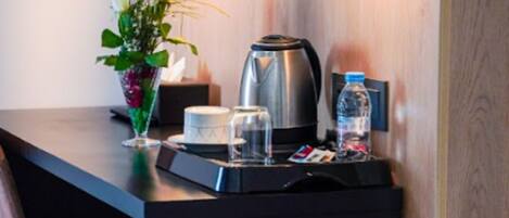 Una kitchenette compacta con cafetera, una botella de agua y un florero con flores sobre la encimera.