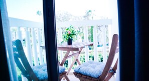 A wooden deck with two chairs and a table, a potted plant, and a white fence in the background.