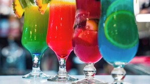 A bar counter with four colorful cocktails, each garnished with a leaf and a mint sprig.